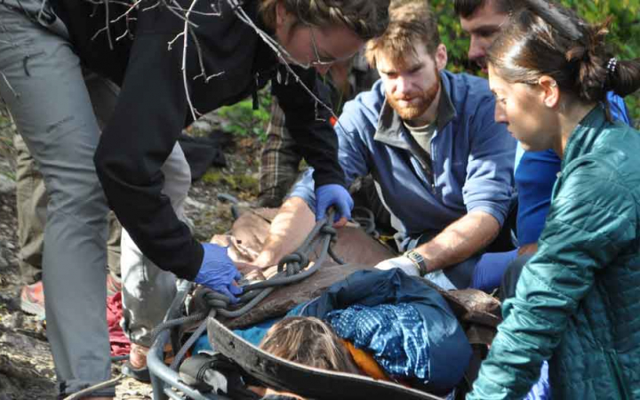a student lays on a stretcher while others tend to him during a wilderness first aid training
